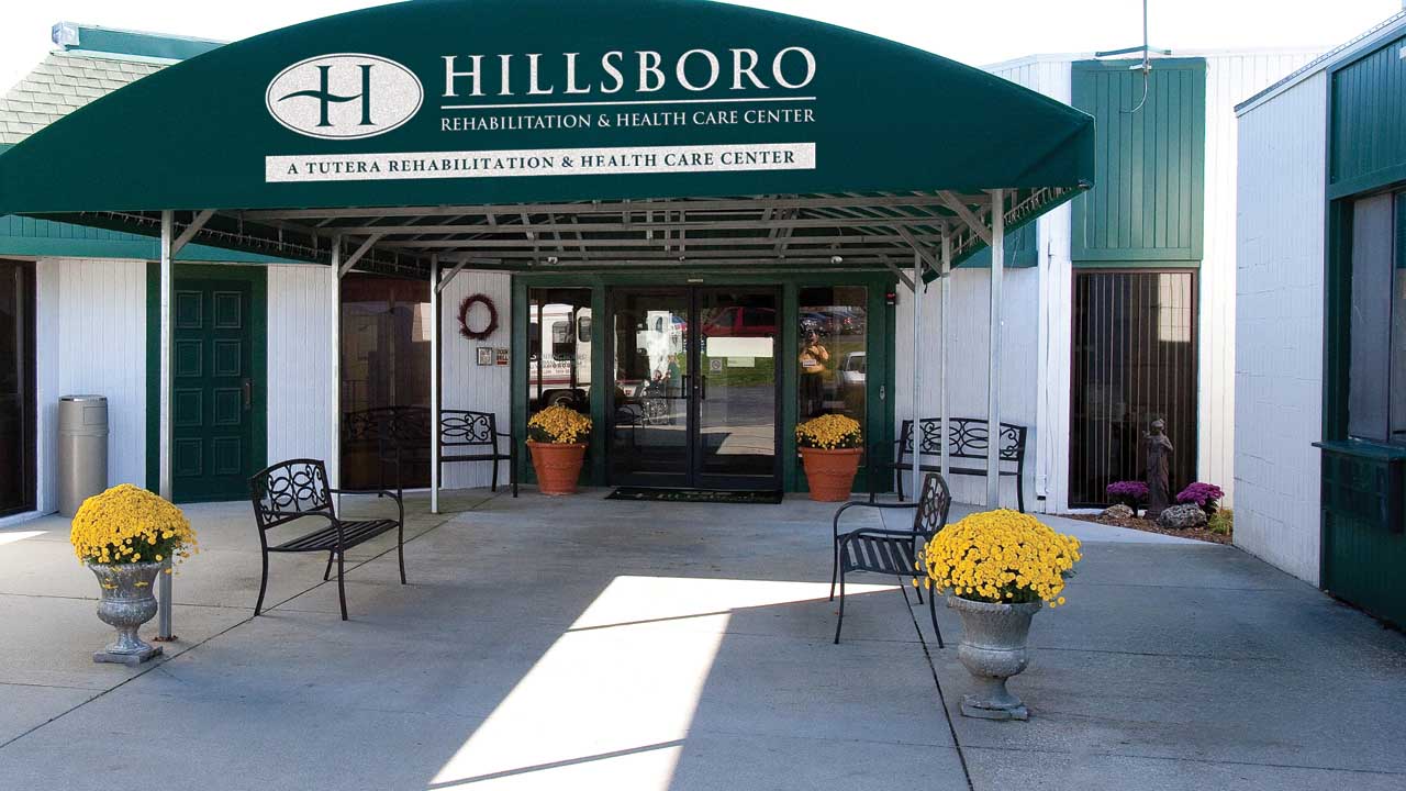 Exterior building view with a large green awning at Hillsboro Rehabilitation &amp; Health Care Center in Hillsboro, IL, Montgomery County.